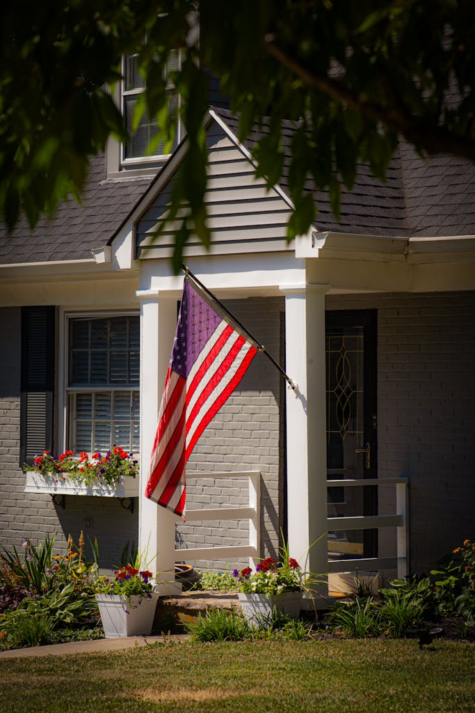A suburban house entrance with a prominently displayed American flag and vibrant flowers.